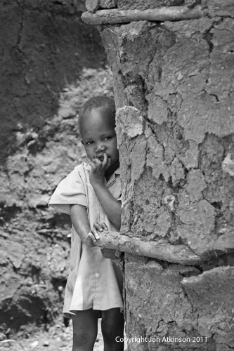 Child outside of dung covered hut, Kenya.